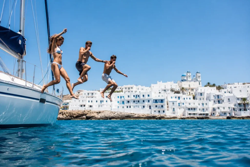Three friends jumping off a sailing yacht near a whitewashed Greek island village
