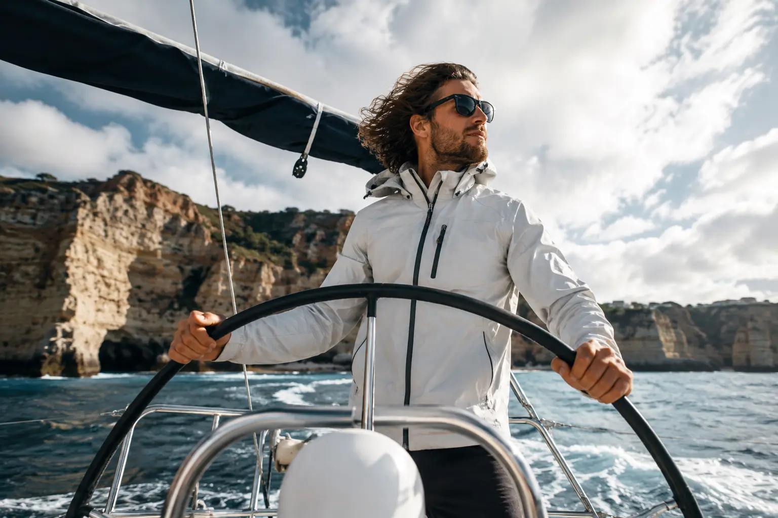 A person steering a sailing yacht near the Algarve cliffs in Portugal